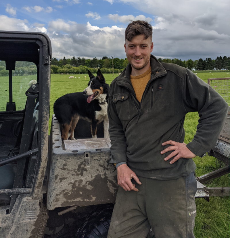 A sheep farming UK worker posing with his dog in front of a tractor